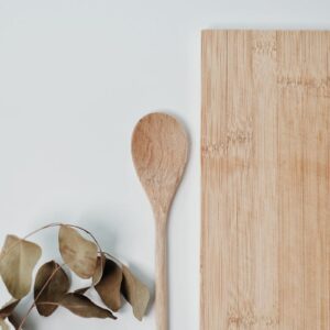 Flat lay of wooden spoon, chopping board, and eucalyptus leaves for eco-friendly kitchen decor.