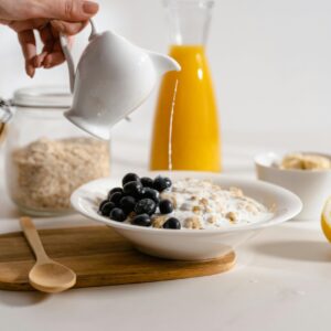A delicious breakfast with oatmeal, blueberries, and milk being poured, accompanied by orange juice.