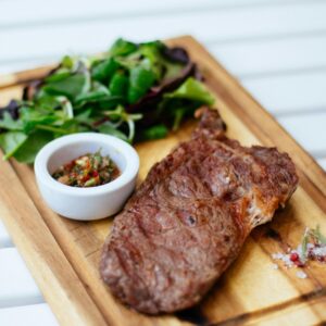 Juicy grilled steak served with fresh herb salad and sauce on a wooden board.