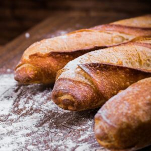 Close-up of fresh, golden-brown baguettes dusted with flour on a wooden table, showing texture and artisan quality.
