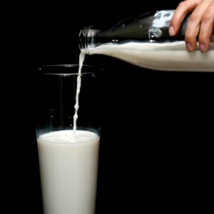 A hand pours fresh milk from a glass bottle into a tall glass with a black backdrop.