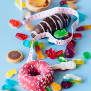 Vibrant and colorful assorted candies, donuts, and pastries alongside a tape measure on a blue background.