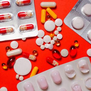 Colorful assortment of pills and tablets spread across a vibrant orange background.